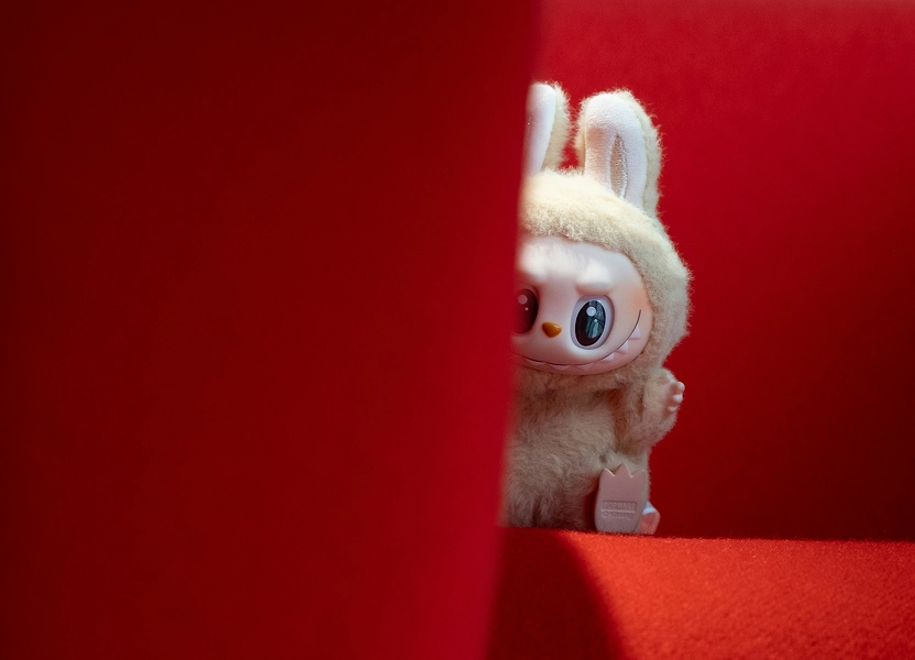 Fluffy rabbit-eared toy peeking around a red display panel